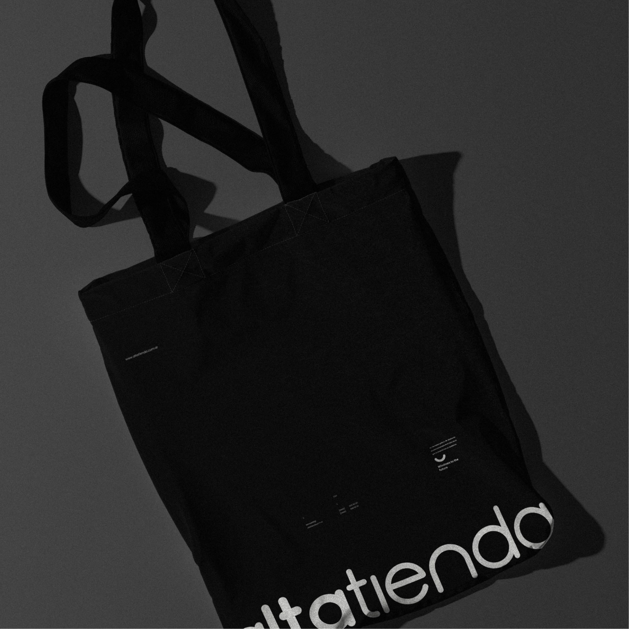 The black tote bag in low light, the wordmark running off the bottom corner