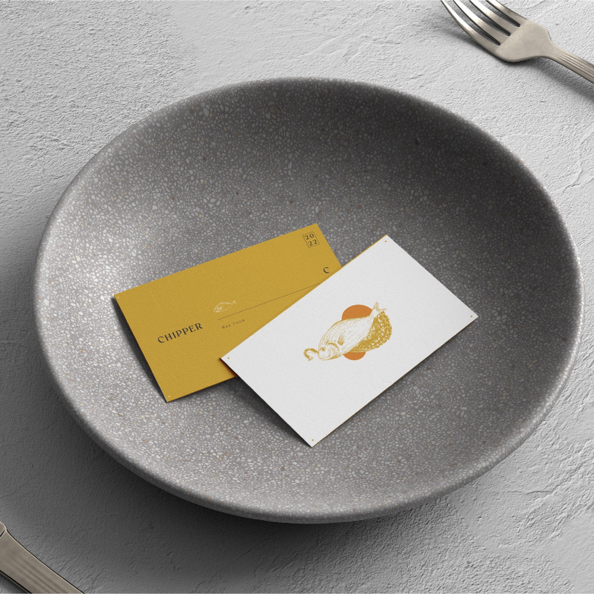 Two business cards, mustard and white, in a stone bowl
