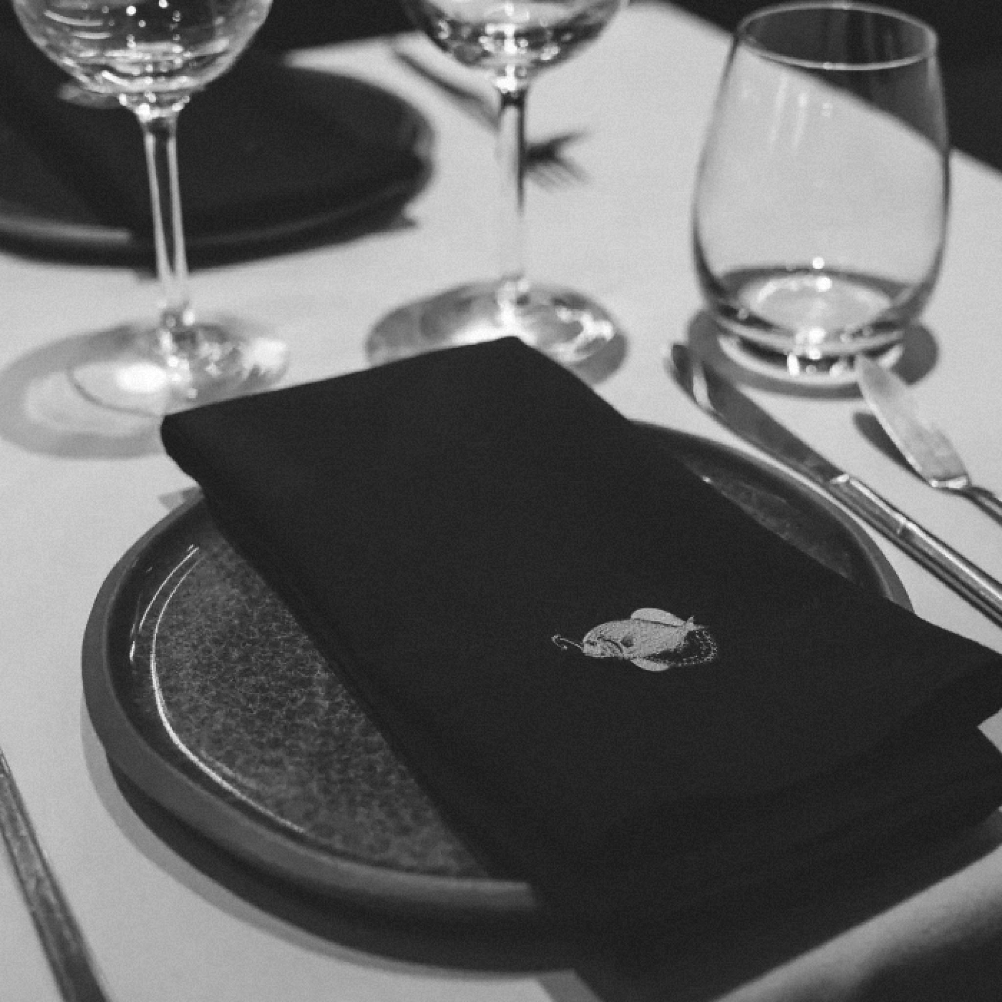 A black napkin with the mark on a dark plate, between wine glasses